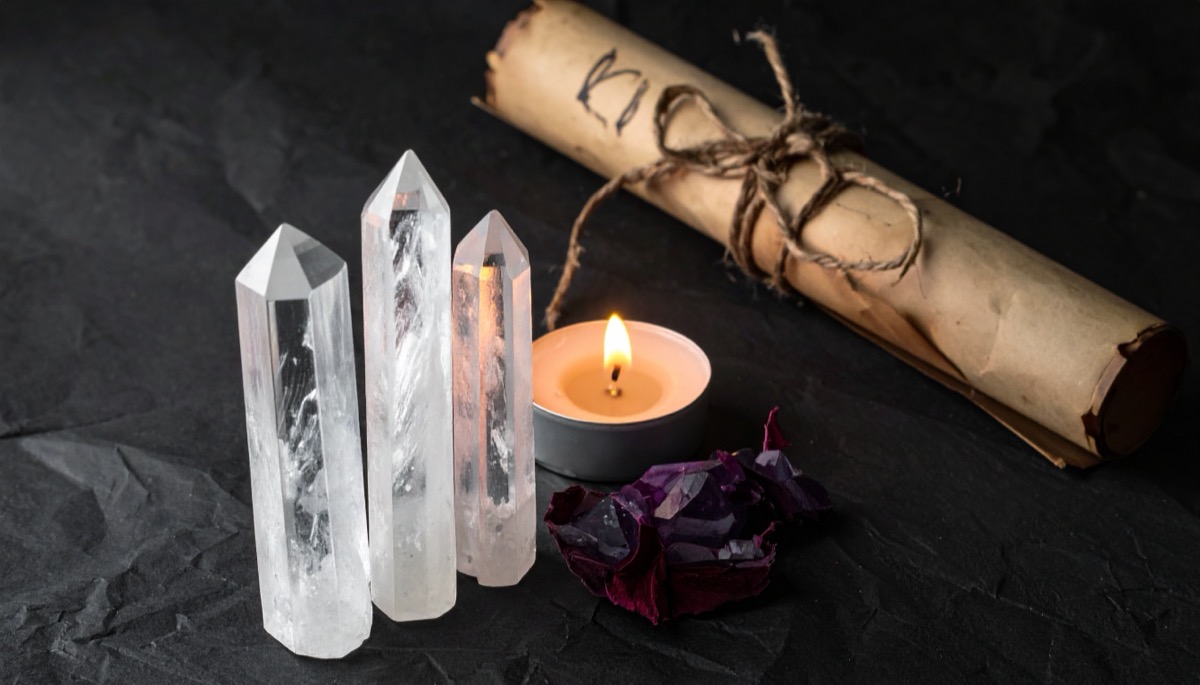 three clear polished points beside a lit tea light, a tied scroll and a dark purple stone