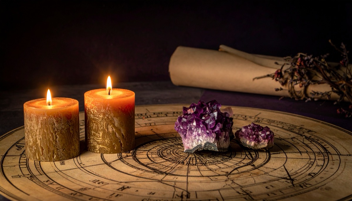 two lit orange pillar candles and purple crystal clusters on an old astrological chart