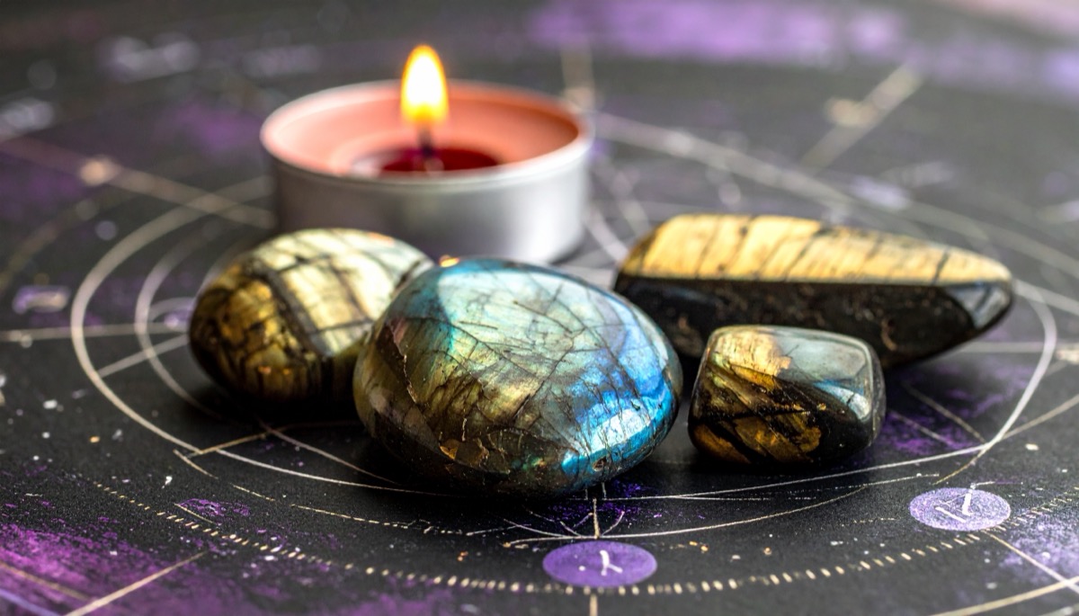four dark polished pebbles flashing blue and gold beside a tea light on a star chart