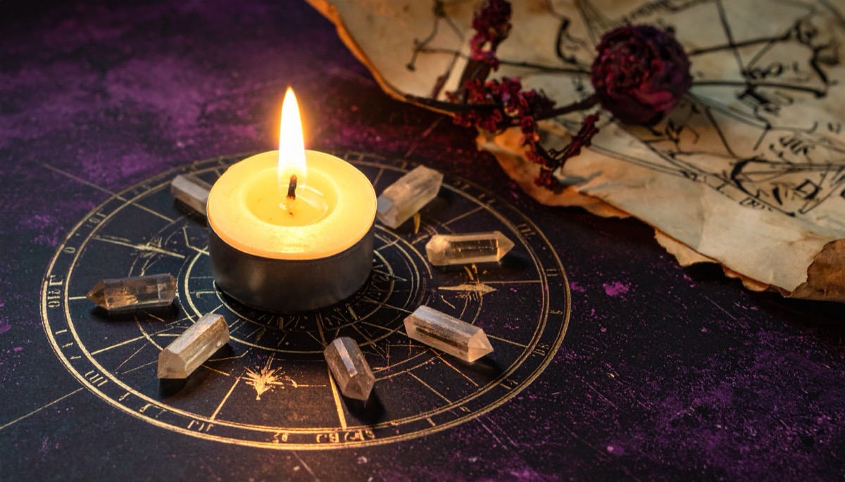 small pale crystal points ringed around a lit tea light on a gold astrological wheel