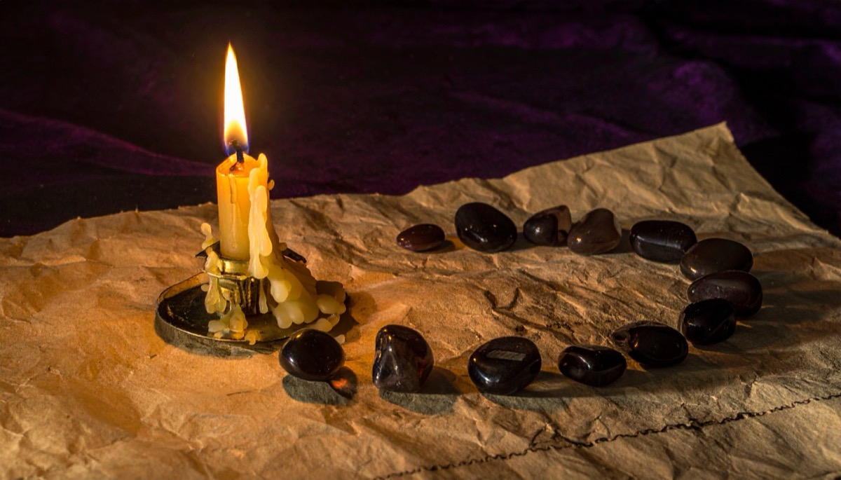 a dripping beeswax candle beside dark tumbled pebbles curving across crumpled brown paper