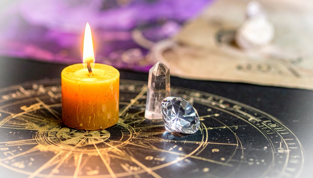 a faceted clear gem and a pale point beside a lit orange candle on a gold zodiac wheel