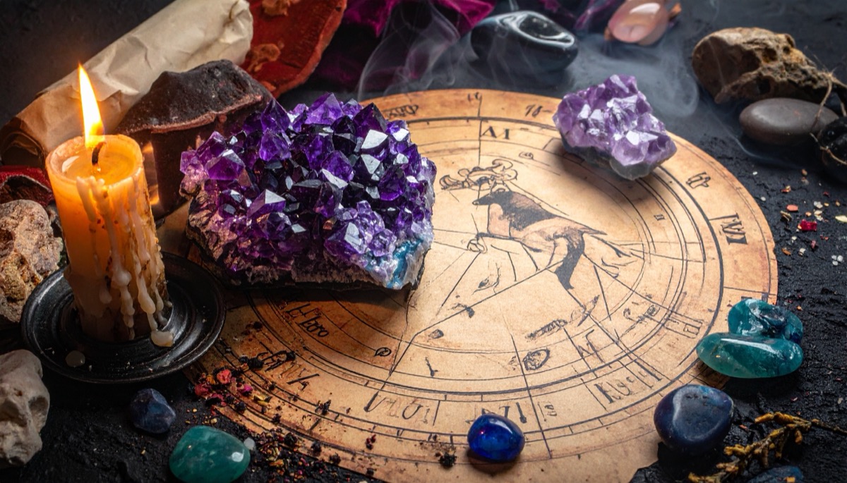 a large deep purple crystal cluster and tumbled stones on a zodiac wheel by candlelight