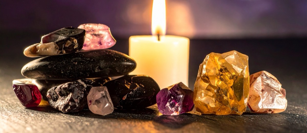stacked dark pebbles and golden rough chunks either side of a lit white candle