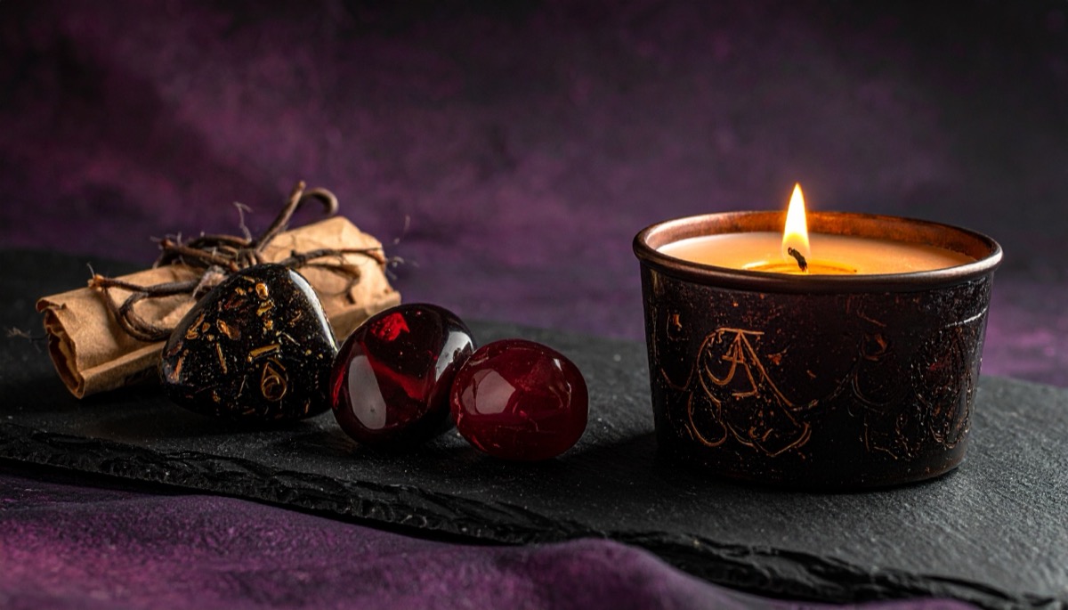 two deep red glassy spheres beside a tied scroll and a dark lit candle on slate