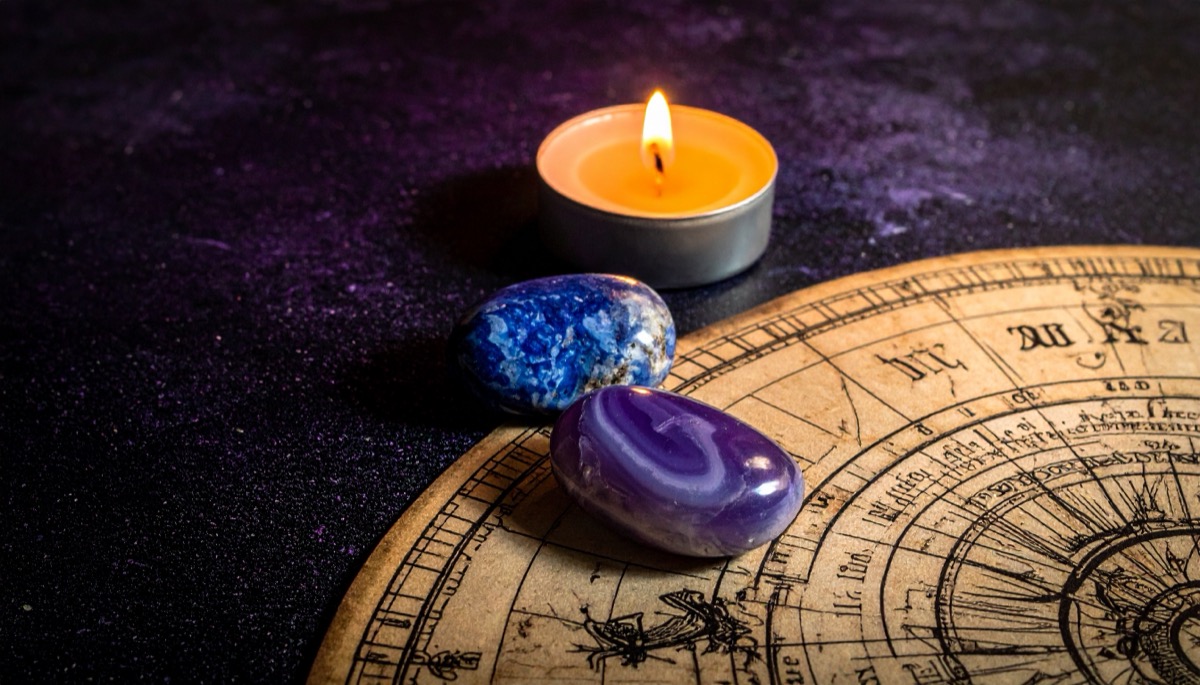 a blue speckled pebble and a banded purple and white pebble on a zodiac wheel by candlelight
