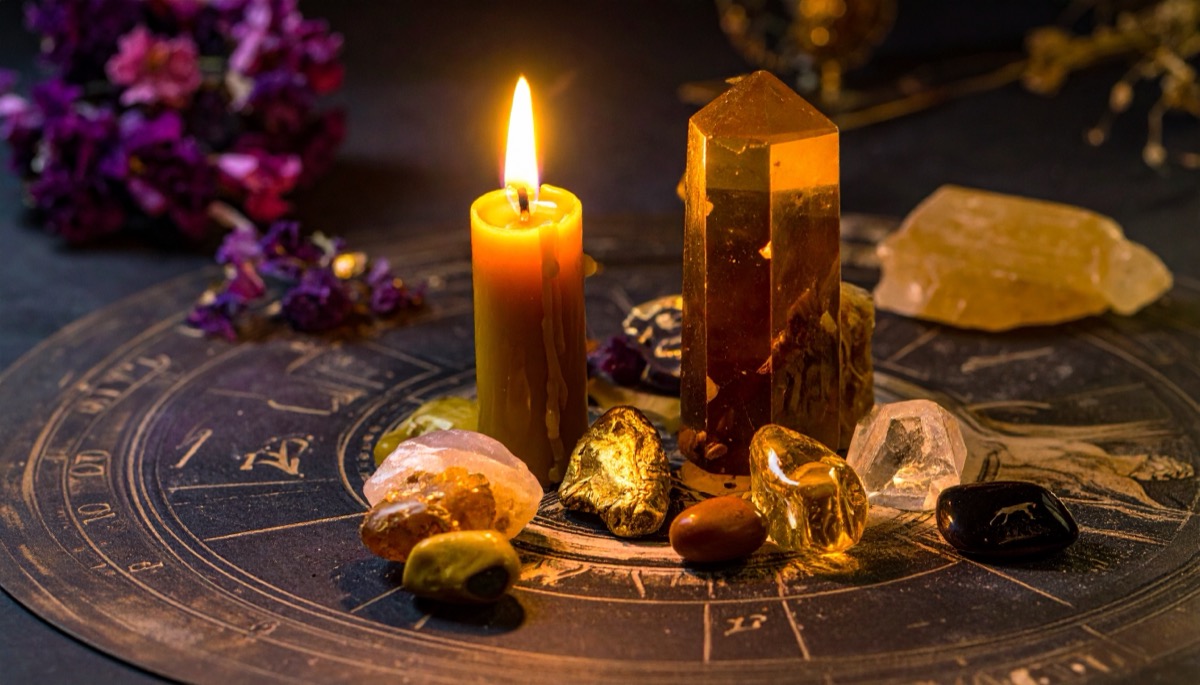 a tall golden orange point and honey coloured tumbled stones on a zodiac wheel by candlelight