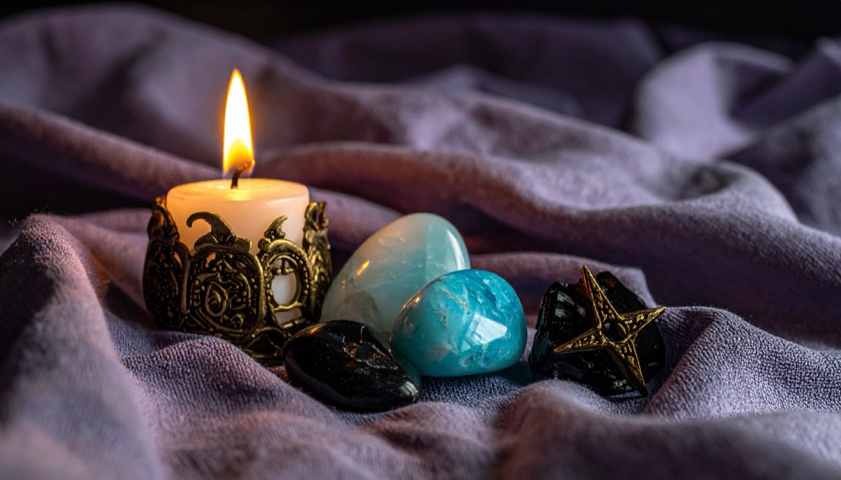 a pale green and a bright blue tumbled stone on soft grey cloth beside a lit candle