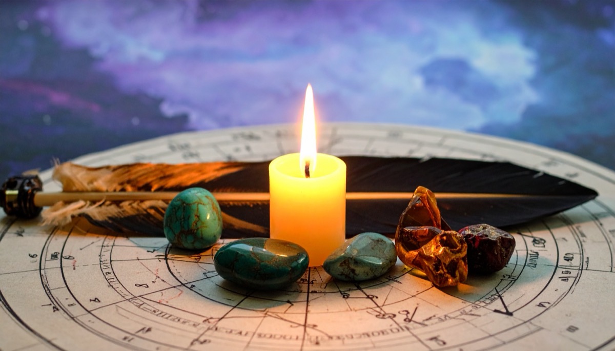 blue green and amber tumbled stones around a lit candle on a chart with a feather