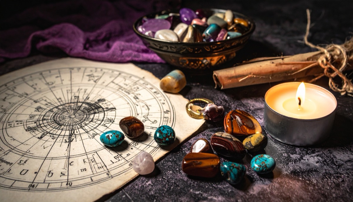 brown and blue green tumbled stones spread across a natal chart beside a bowl and tea light