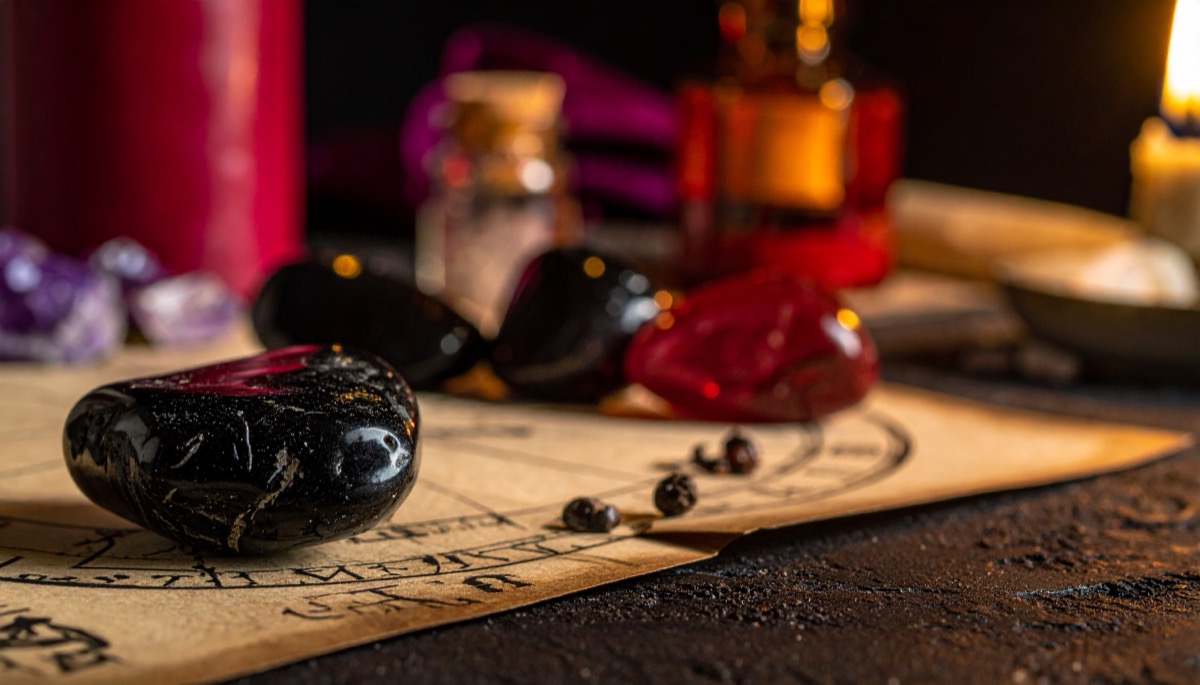 a glossy black tumbled stone and a red stone on inked parchment with dark apothecary bottles