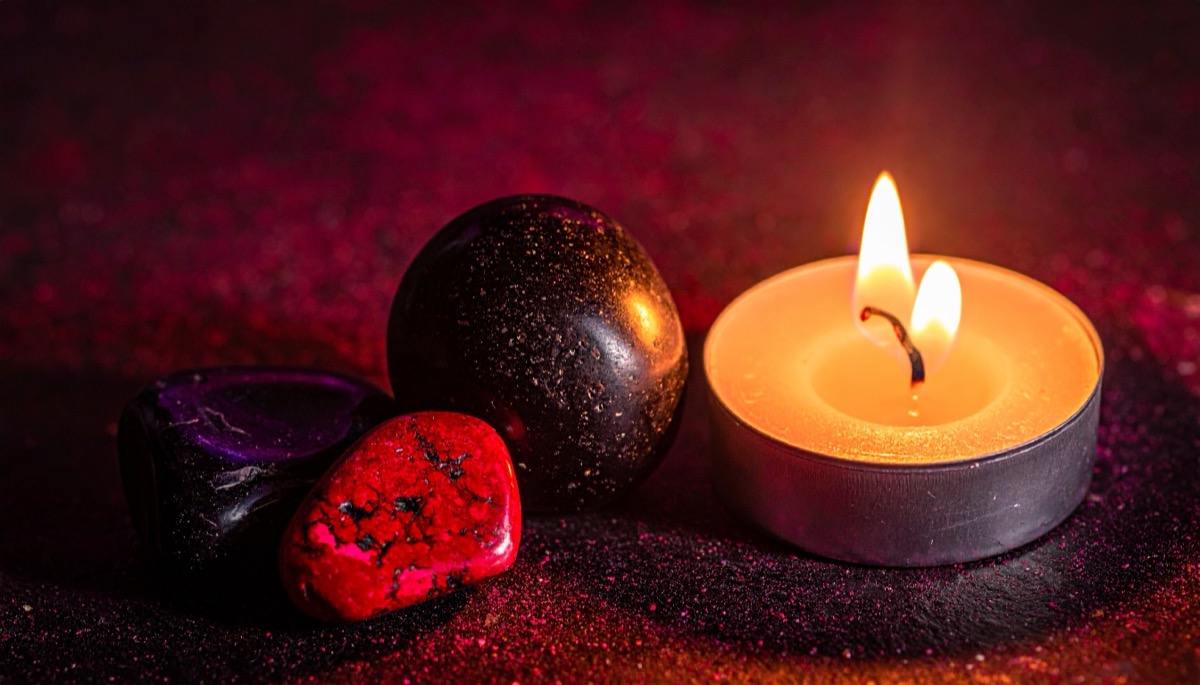 a black sphere with red and purple tumbled stones beside a tea light on red sand