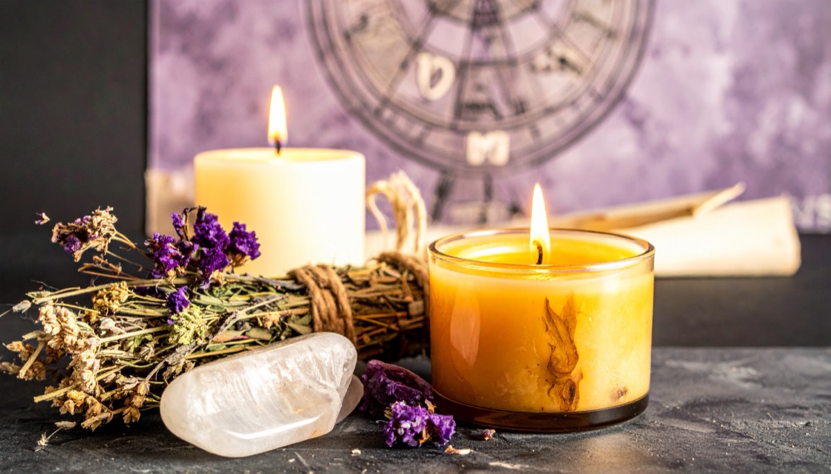 a milky white palm stone with dried purple flowers and two lit candles before a zodiac wheel