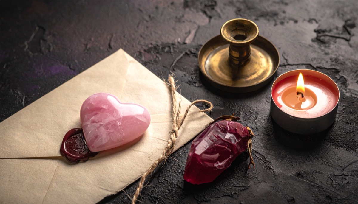 a pink heart shaped polished stone on a sealed envelope with a brass holder and tea light