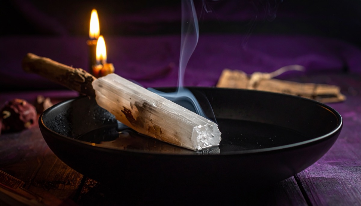 a fibrous white stick shaped stone smoking in a black bowl beside two lit candles