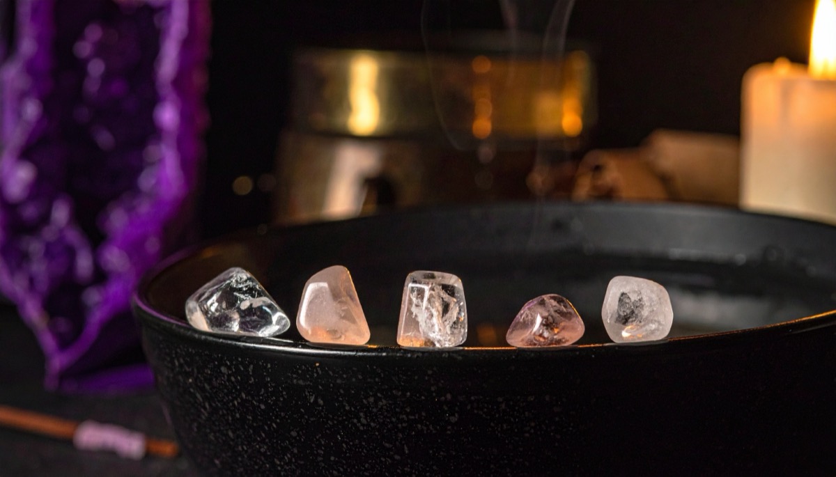 five clear and pale pink tumbled stones lined along the rim of a black bowl of water