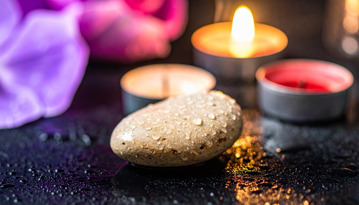 a pale speckled pebble covered in water droplets in front of three lit tea lights