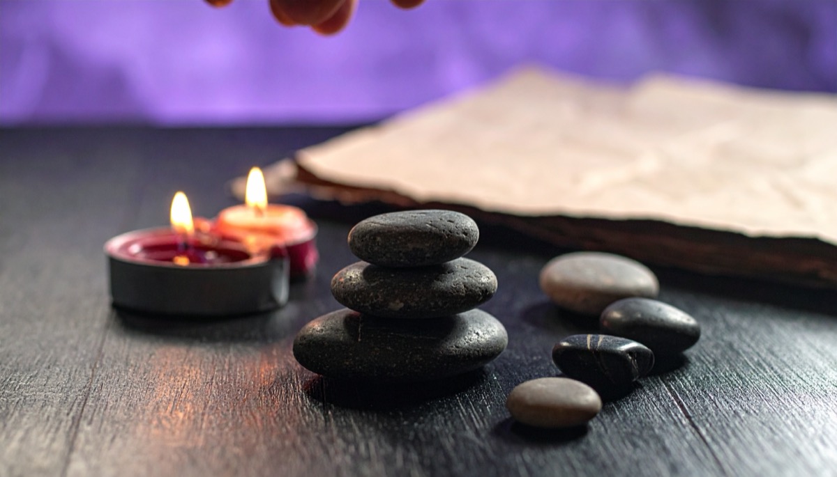 a stack of smooth dark grey pebbles on a dark table beside two lit tea lights
