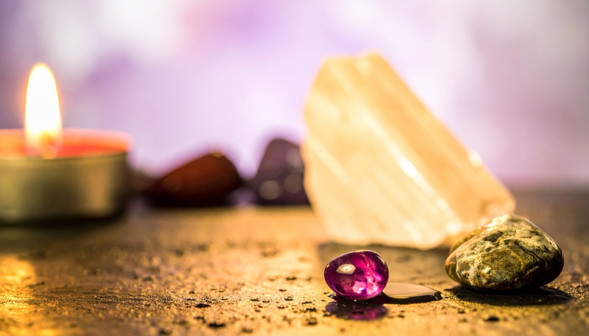a pale honey coloured rough slab, a pink cabochon and tumbled stones beside a tea light
