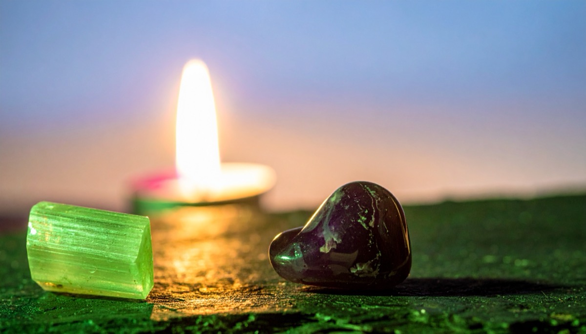 a pale green rough crystal and a dark purple tumbled stone on green stone by candlelight
