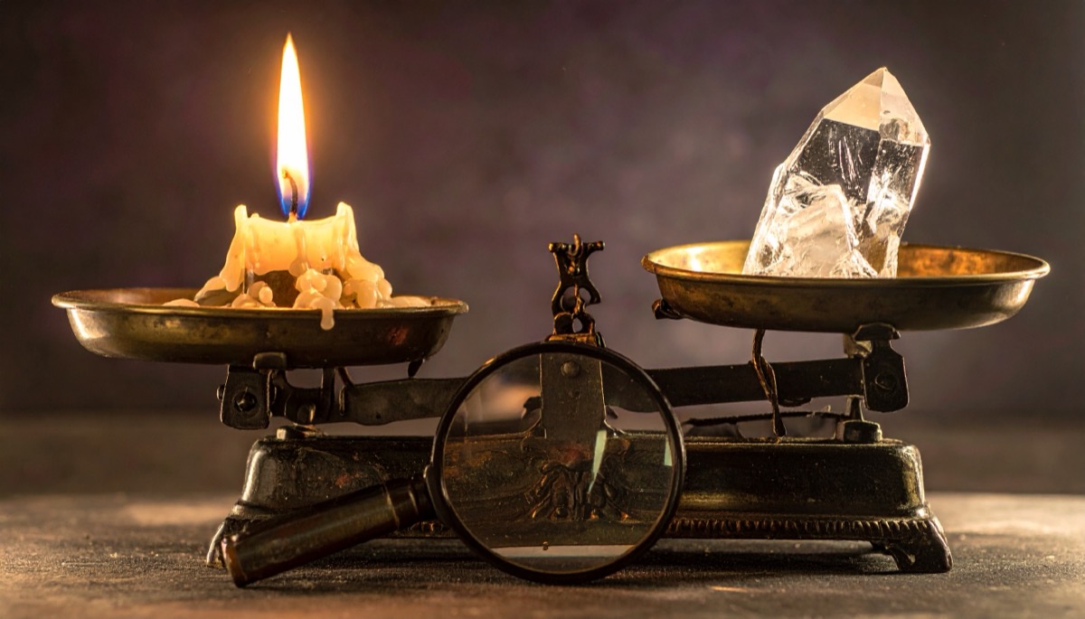 a clear crystal point on brass balance scales weighed against a candle, with a magnifier