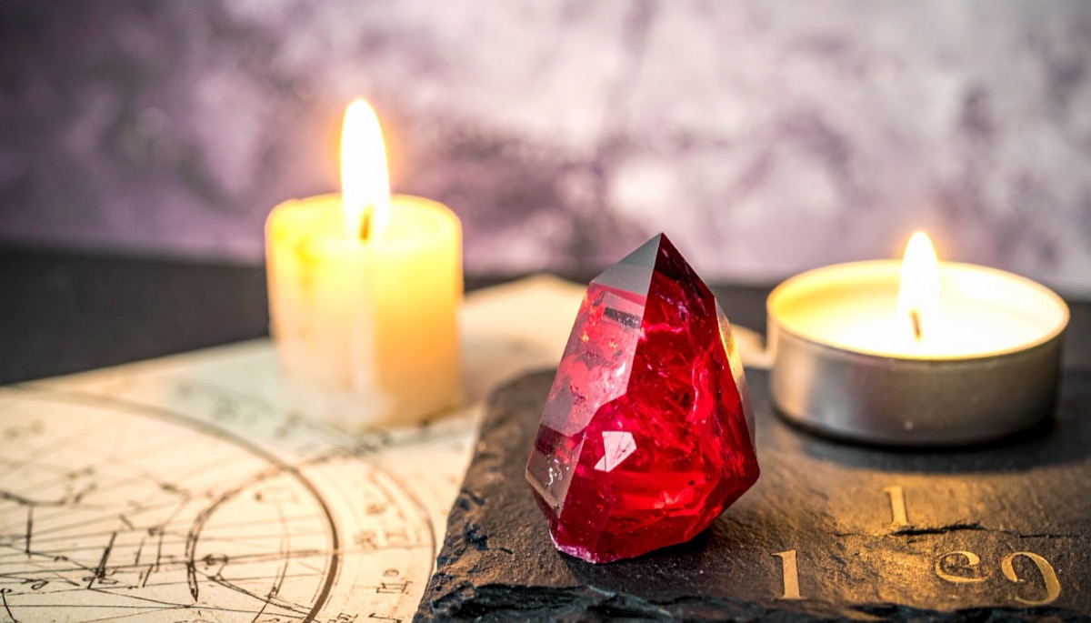 a faceted deep red gem on slate between two lit candles on an old chart
