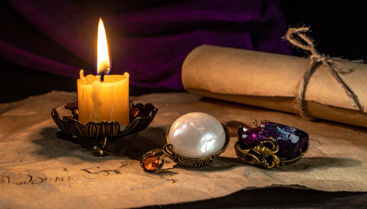 a lustrous white domed cabochon and a purple stone in gold settings on aged paper