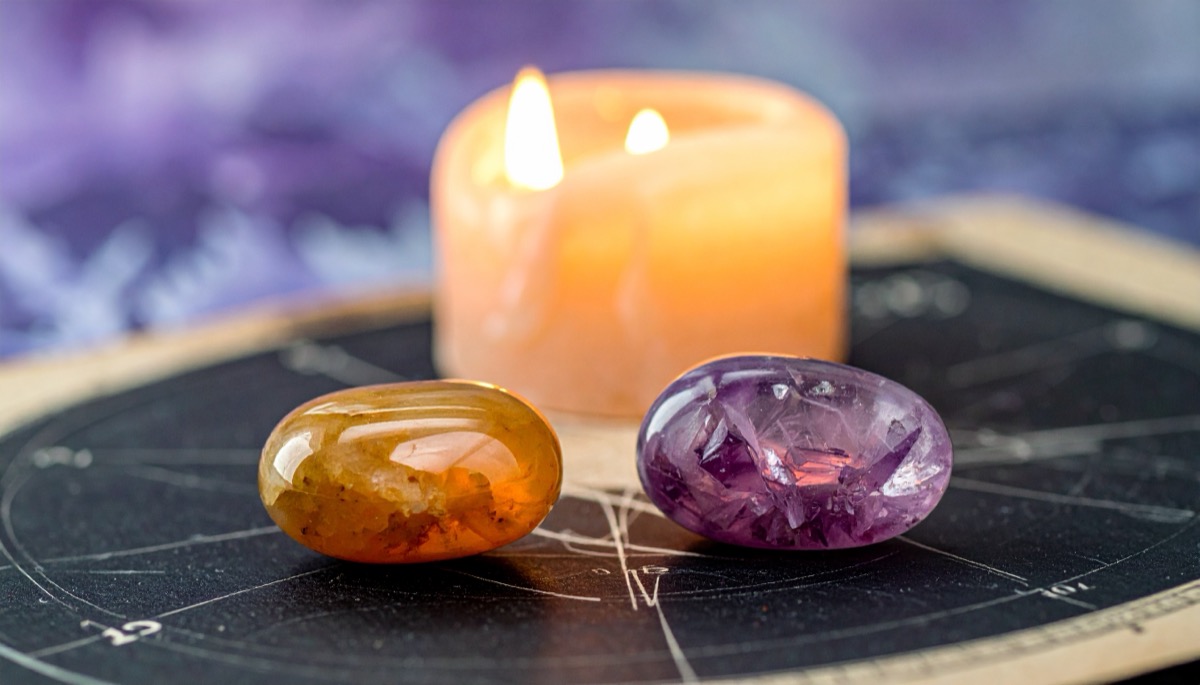 an amber tumbled stone and a purple tumbled stone side by side on a chart before a candle