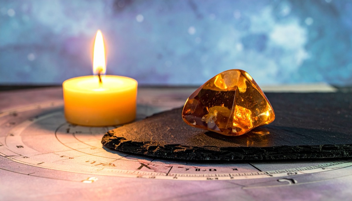 a warm amber polished stone on a black disc beside a lit tea light on a chart