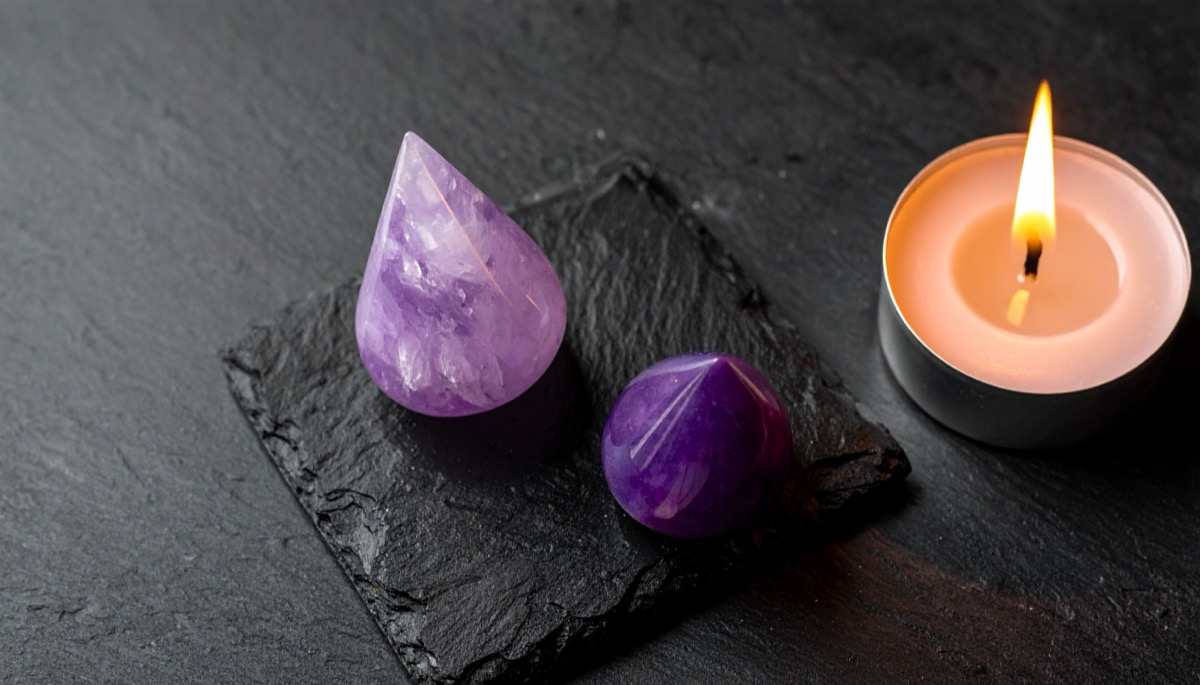a pale lilac teardrop and a darker faceted purple bead on slate beside a tea light