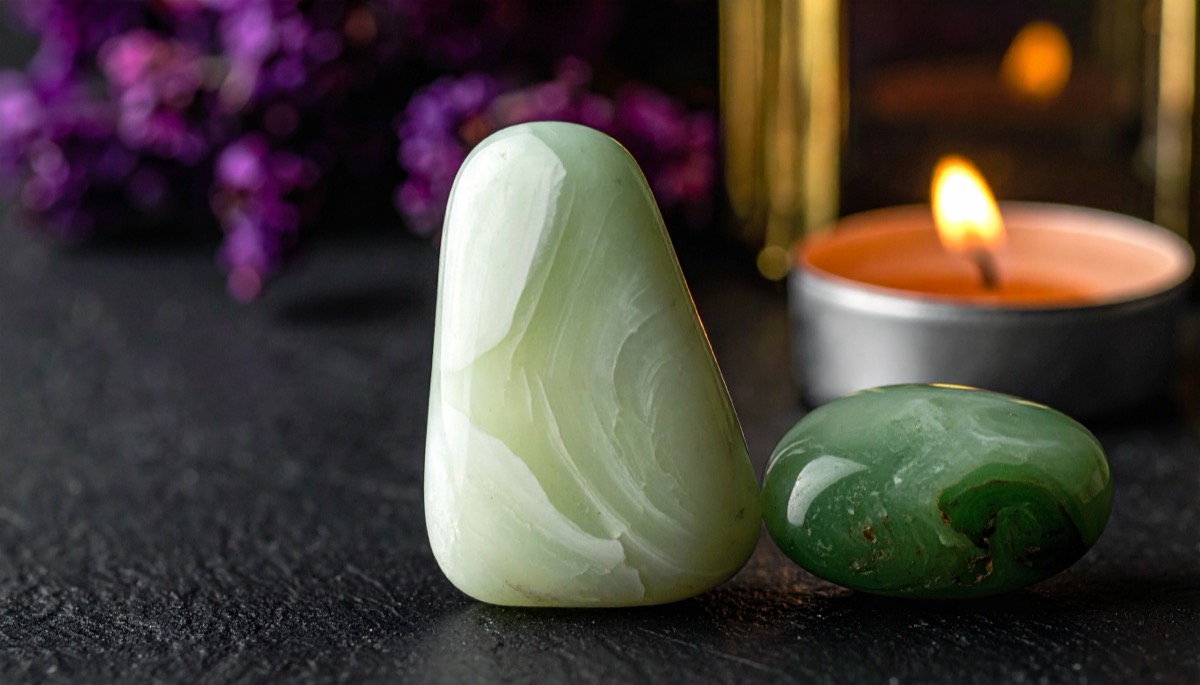 a creamy pale green tumbled stone next to a deeper green pebble beside a lit tea light