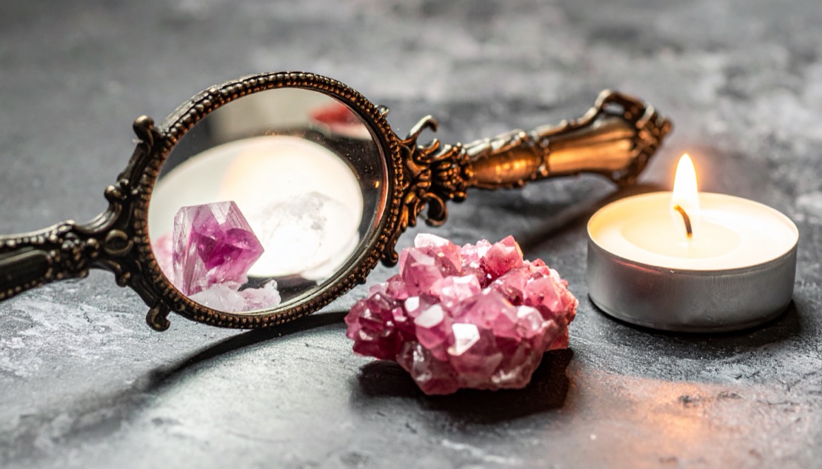 a pink druzy cluster in front of an ornate hand mirror reflecting stones, beside a tea light