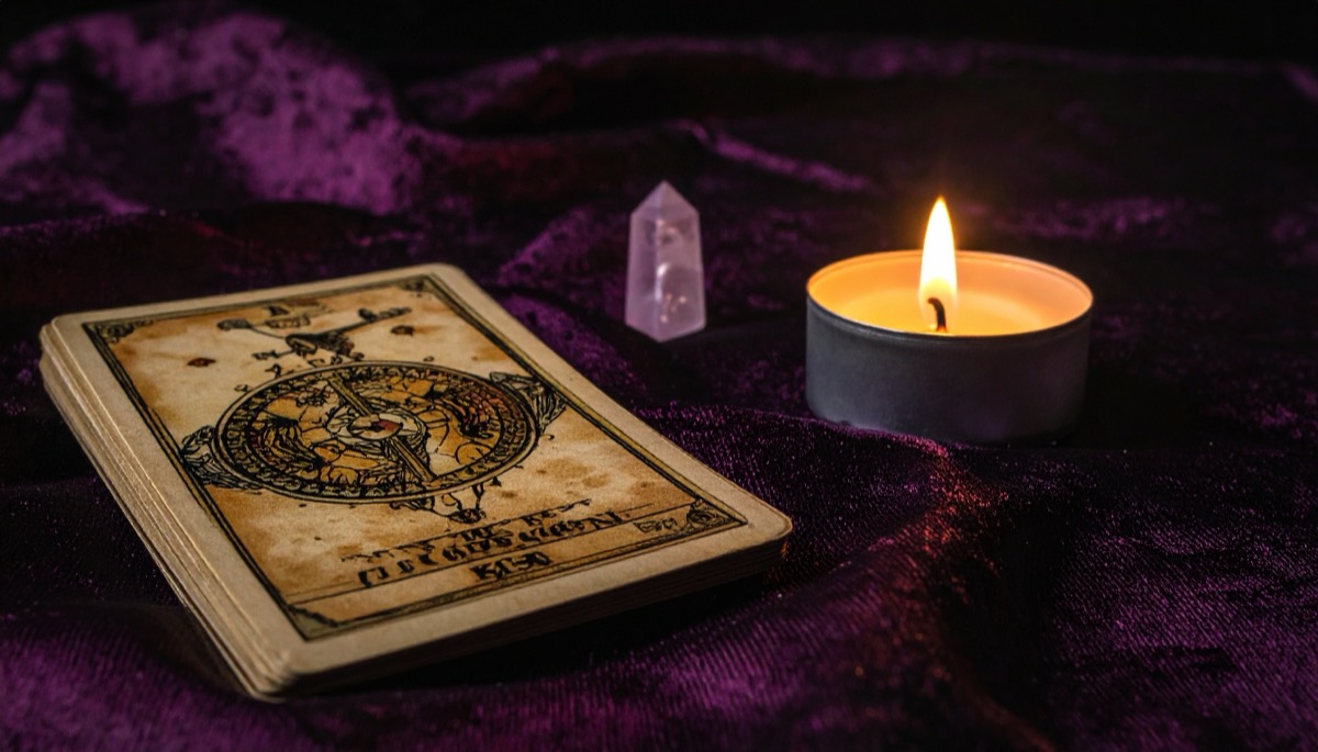 one aged illustrated tarot card face up on purple velvet with a small point and tea light