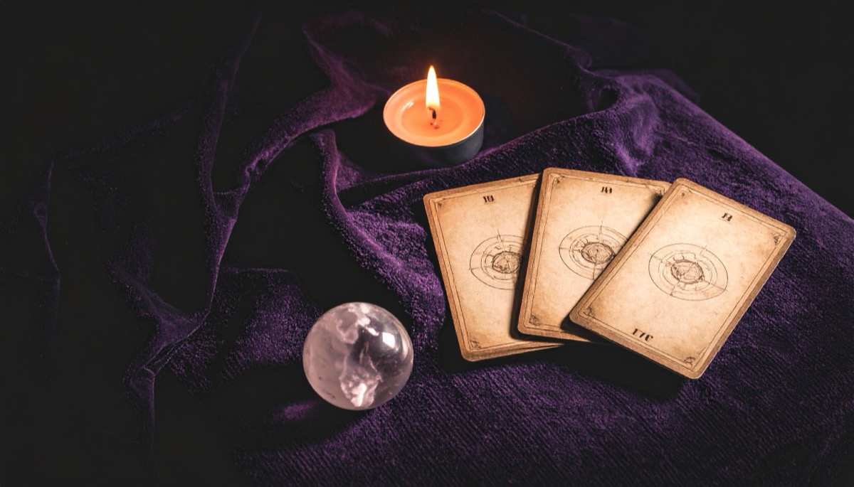 three face down tarot cards fanned on purple velvet with a clear sphere and a tea light