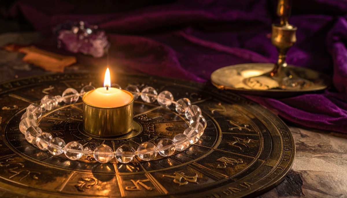 a ring of clear round beads circling a lit tea light on an engraved brass zodiac disc
